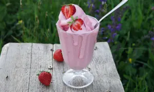 Un cremoso gelato alla fragola, guarnito con fragole fresche, su un tavolo di legno rustico, con un prato fiorito sullo sfondo.