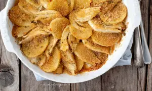 Finoçchi gratinati al forno, dorati e croccanti, in una pirofila bianca su un tavolo di legno.
