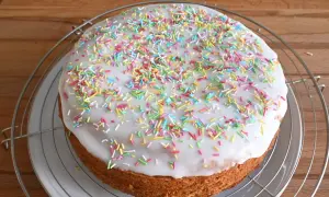 Torta rotonda con glassa di zucchero bianca e confettini colorati, su una griglia metallica.