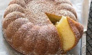 Una torta semplice e veloce, soffice e spolverata di zucchero a velo, con una fetta tagliata che ne mostra l'interno dorato.