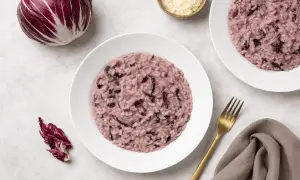 Un cremoso risotto al radicchio rosso, con un cespo intero e foglie sparse, pronto per essere gustato.