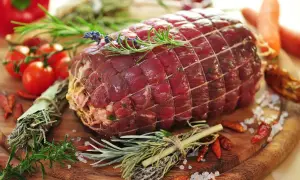 Un succulento arrosto di manzo, legato con spago e guarnito con rosmarino e lavanda, pronto per essere cucinato con pomodorini, peperoncini e carote.
