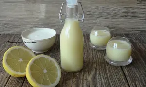 Una bottiglia e due bicchierini di crema di limoncello, con limoni freschi e una ciotola di panna.