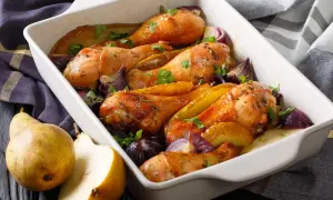 Cosce di pollo al forno croccante con pere e cipolle rosse in una teglia bianca.