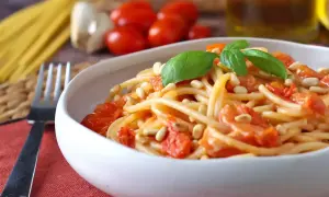 Un piatto invitante di spaghetti con pomodorini freschi, pinoli tostati e basilico, pronto per essere gustato.