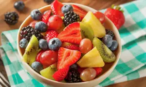 Una ciotola piena di macedonia di frutta colorata: fragole, mirtilli, lamponi, kiwi, ananas e uva.