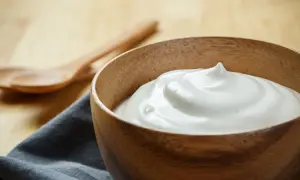 Una ciotola di legno piena di soffice crema al latte, pronta per essere gustata. Due cucchiai di legno sullo sfondo.