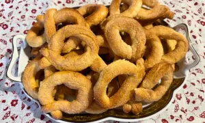 Un piatto pieno di torcetti al burro, dorati e zuccherati, pronti per essere gustati.