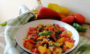 Un piatto colorato di peperonata con melanzane, pomodori e peperoni, guarnito con basilico fresco. La ricetta perfetta per un contorno estivo.