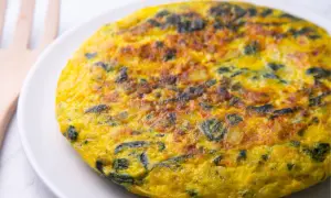 Frittata di spinaci dorata e soffice su un piatto bianco, con un utensile in legno sullo sfondo.