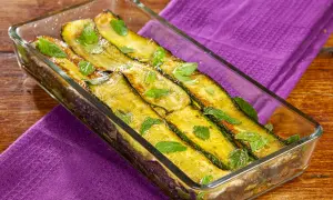 Zucchine alla scapece dorate e profumate, guarnite con foglie di menta fresca in una pirofila di vetro su un tavolo di legno.
