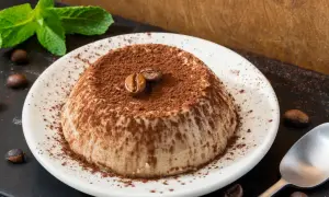 Deliziosa panna cotta al caffè, cosparsa di cacao e decorata con chicchi di caffè e menta fresca.