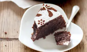 Una fetta di torta caprese ricetta facile, cosparsa di zucchero a velo e cacao, su un piatto bianco a forma di cuore.