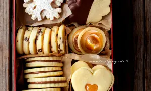 Scatola piena di biscotti al burro: a fiocco di neve, con gocce di cioccolato, ripieni di caramello, a forma di cuore e ricoperti di cioccolato.