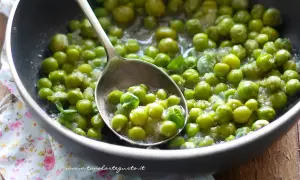 Piselli freschi in padella, cotti con cipolla e menta. Un cucchiaio ne raccoglie una porzione invitante.