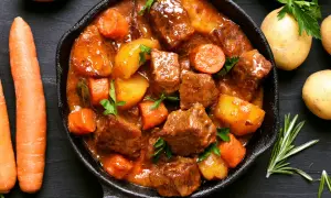 Un saporito spezzatino di maiale in padella con patate e carote, guarnito con prezzemolo fresco.