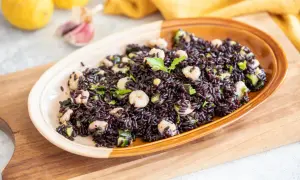 Un invitante piatto di riso venere con gamberetti, zucchine e prezzemolo, guarnito con un ciuffo di erbe aromatiche.