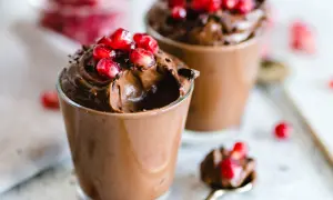 Due bicchierini di golosa mousse al cioccolato, guarniti con chicchi di melagrana e scaglie di cioccolato.