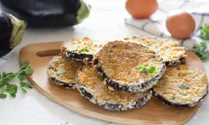 Fette di melanzane al forno impanate, dorate e croccanti, guarnite con erbe aromatiche fresche.