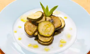 Fette di zucchine alla scapece, condite con olio e guarnite con menta fresca, su un piatto bianco.