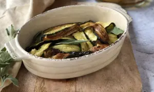 Zucchine in carpione dorate e saporite, guarnite con foglie di salvia fresca, servite in una ciotola rustica.