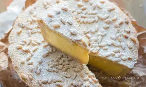 Torta della nonna facile, con crema gialla, pinoli e zucchero a velo. Una fetta è stata tagliata.