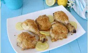 Cosce di pollo al limone croccanti e dorate, servite su un piatto bianco con fette di limone fresco.