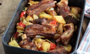 Puntine di maiale succulente al forno con patate, peperoni e cipolle in una teglia scura.
