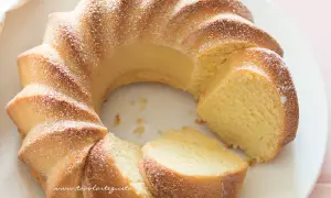 Una torta di ricotta sofficissima, dorata e cosparsa di zucchero a velo, tagliata a fette su un piatto bianco.