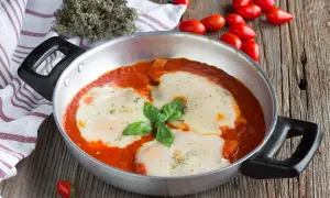 Un invitante pollo alla pizzaiola in padella, con mozzarella filante e basilico fresco, pronto per essere gustato.