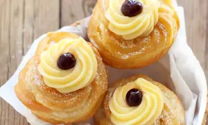 Tre zeppole di San Giuseppe, dolci fritti con crema pasticcera e ciliegina, spolverate di zucchero a velo.