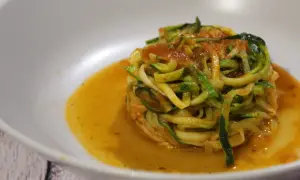 Un piatto di spaghetti di zucchine conditi con sugo rosso, serviti in una ciotola bianca.