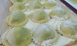 Un vassoio pieno di ravioli ricotta e spinaci freschi, spolverati di farina, pronti per essere cucinati.