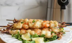 Spiedini di gamberi e calamari impanati, cotti alla perfezione nella friggitrice ad aria, serviti su un letto di insalata con spicchi di limone.