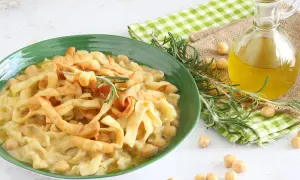 Piatto di ciceri e tria, pasta fresca con ceci, guarnito con rosmarino e croccanti straccetti fritti. Olio d'oliva e ceci sparsi intorno.