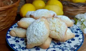 Biscotti con farina di mandorle, spolverati di zucchero a velo, su un piatto decorato. Sullo sfondo limoni e un cestino.