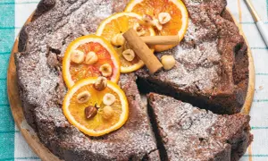 Torta di pane al cioccolato, decorata con fette d'arancia, nocciole e cannella, spolverata di zucchero a velo.