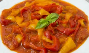 Peperonata ricetta della nonna: peperoni rossi e gialli cotti lentamente in un sugo saporito, guarniti con una foglia di basilico fresco.