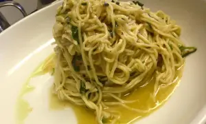Un piatto di spaghetti aglio olio e peperoncino cremosi, conditi con prezzemolo fresco e un filo d'olio d'oliva, serviti in una ciotola bianca.