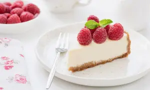 Una fetta di torta fredda allo yogurt, guarnita con lamponi freschi e menta, su un piatto bianco.