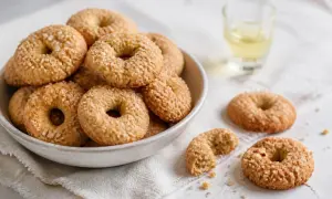 Ciambelline al vino friabilissime, dorate e cosparse di zucchero, in una ciotola e sparse su un panno, con un bicchierino di vino.