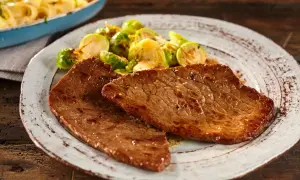 Due fette di paillard di vitello succulento servite con cavolini di Bruxelles arrostiti e un contorno di pasta in un piatto rustico.