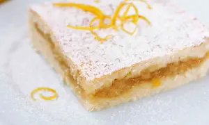 Una fetta di torta con pasta frolla morbida, ripiena di marmellata e spolverata di zucchero a velo e scorza d'arancia.