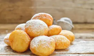 Pile di frittelle di zucca dorate e soffici, cosparse di zucchero a velo, su un tavolo di legno rustico.