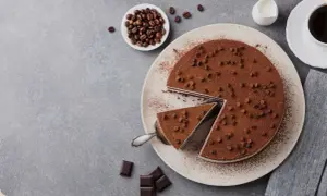 Una deliziosa torta al caffè, cosparsa di cacao e gocce di cioccolato, con una fetta servita. Chicchi di caffè e cioccolato completano la scena.