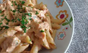 Penne al baffo cremose e saporite, condite con una salsa rosa e prezzemolo fresco, servite su un piatto decorato con fiori.