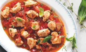 Piatto di coniglio alla cacciatora ricetta della nonna, con pezzi di carne tenera in salsa di pomodoro e peperoni, guarnito con basilico fresco e timo.