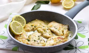 Scaloppine al limone cremose in padella, guarnite con spicchi di limone fresco e prezzemolo tritato.