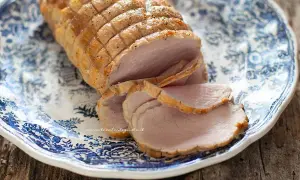Arrosto di maiale morbido con sughetto, affettato su un piatto decorato con motivi blu. Perfetto per un pranzo domenicale.