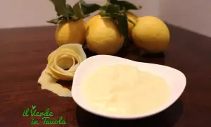 Una ciotola di cremosa crema al limone, con limoni freschi e una decorazione a forma di rosa fatta con la scorza.